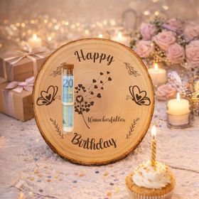 Geburtstags-Baumscheibe mit Holzgravur, verziert mit bunten Schmetterlingen aus gefalteten Geldscheinen, arrangiert in warmem Ambiente mit Kerzen und Blumen.