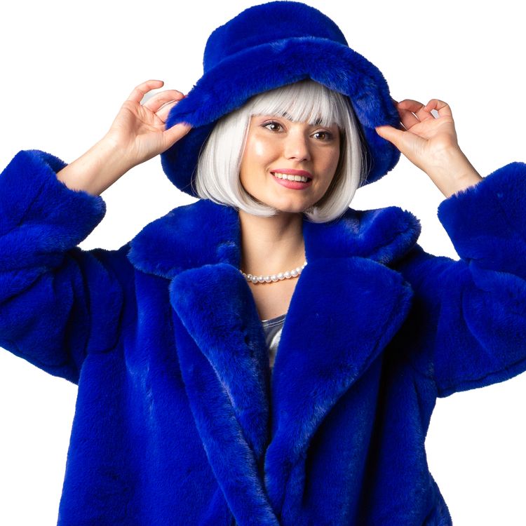 Dame trägt royalblaue Plüschjacke im 90er-Retro-Look mit passendem Plüschhut, schwarze Hose und silberne Pumps vor weißem Hintergrund.