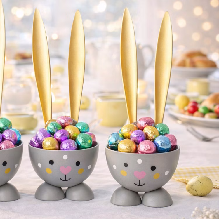 Eierbecher-Set 6 Stück Hase Gold aus Metall Osterhase gedeckter Tisch Ostern Oster-Deko Dekoration Frühling Osterfest Osterbrunch Tisch-Deko Graue Hasen-Eierbecher mit langen goldenen Ohren, gefüllt mit bunten Schokoladeneiern in glänzender Folie, auf einem festlich dekorierten Osterbrunch-Tisch.