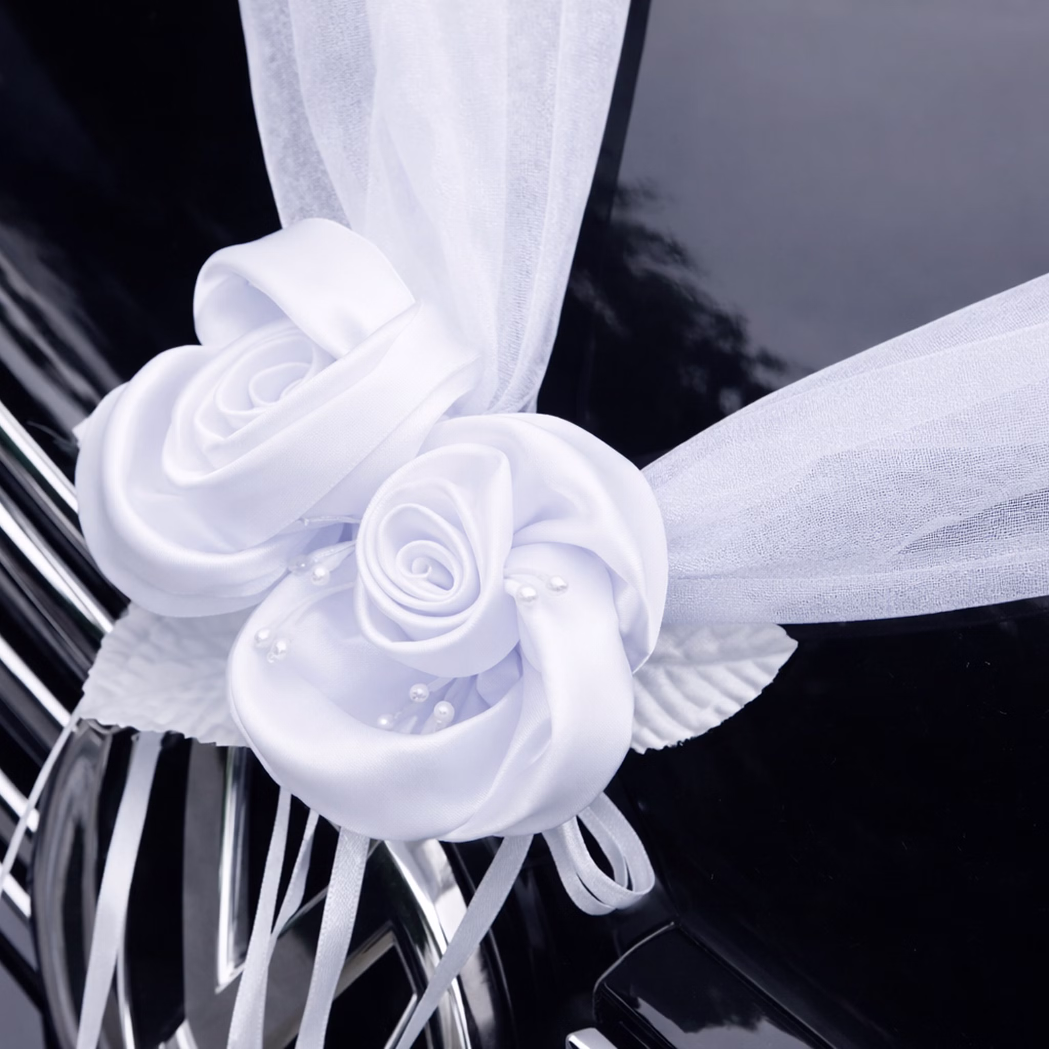 Autoschmuck Deko 2 Girlanden mit Blüten Weiß 180 cm Motorhaube Hochzeitsauto Wedding Car Organza-Girlande mit Rosenblüten Dekoration Nahaufnahme einer weißen Organza-Girlande mit zwei dekorativen Rosenblüten auf der Motorhaube eines schwarzen Autos befestigt.