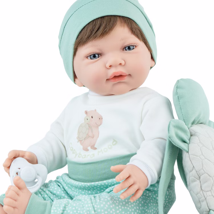 Puppe Mila 42 cm beweglich mit Softbody, Schnuller & Schildkröten-Rucksack Spielpuppe Spielzeug Spielwaren für Kinder Geschenkidee Detailansicht Puppe Mila Gesicht und Bekleidung mit niedlichem Capybara auf dem Oberteil sitzend seitlich von Vorne.