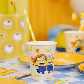 Minions Partybecher auf blau karierter Tischdecke mit gelbem Teller, Bananenmotiven und farbenfroher Geburtstagsdekoration.