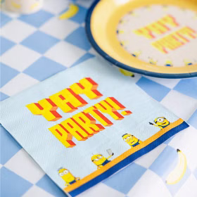 Minions Yay-Party-Serviette auf blau karierter Tischdecke mit gelbem Partyteller und fröhlichen Bananenmotiven dekoriert.