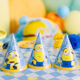 Minions Partyhüte Geburtstagstisch Drei blaue Minions Partyhütchen mit verschiedenen Motiven auf einer karierten Geburtstagstafel mit farbiger Dekoration.