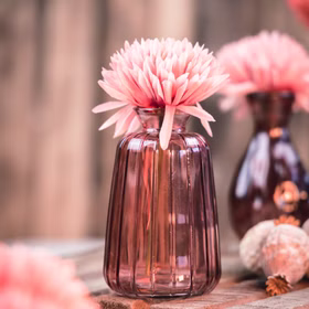 Glasvase Verone 11 cm Vintage Tischvase Rosa Grün Transparent Deko Geburtstag Tisch-Deko Hochzeit Geburtstag Vase aus Glas festliche Tischdeko Wohnaccessoire Glasvase dekorativ Rosa Glasvase Verone mit rosafarbener Blüte auf rustikalem Holztisch, im Hintergrund weitere Vasen in weicher Unschärfe.
