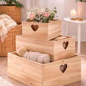 3er Set Holzkisten mit Herz im Wohnambiente, dekorativ gefüllt mit Handtüchern und Blumen.