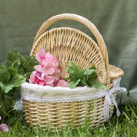 Picknickkorb aus Naturweide mit Blumenfüllung, auf Gras vor grünem Hintergrund..
