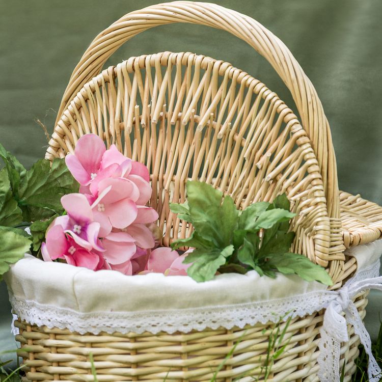 Geflochtener Picknickkorb aus Weide mit geöffnetem Deckel und hellem Stoffeinsatz mit Spitze.
