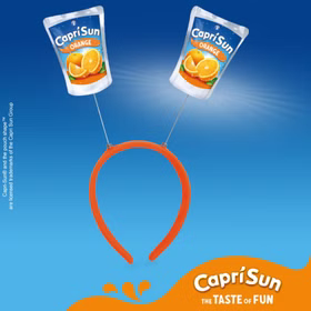 Oranger Capri-Sun® Haarreif mit zwei wackelnden Orange-Trinkpäckchen-Motiven vor blauem Hintergrund mit Capri Sun Branding.