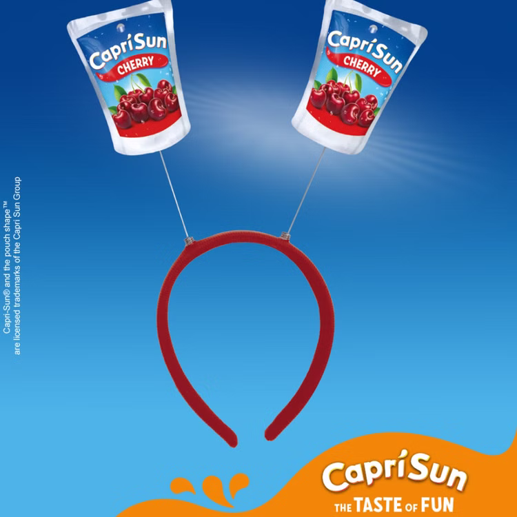 Capri Sun Cherry Haarreif Party Accessoire Roter Capri-Sun® Cherry Haarreif mit zwei wackelnden Trinkpäckchen-Motiven vor blauem Hintergrund mit Capri Sun Branding.