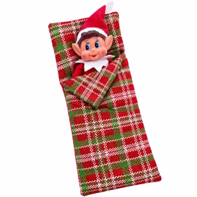 Wichtel Schlafsack mit Wichteljunge Fröhlicher Wichteljunge mit roter Zipfelmütze liegt eingekuschelt im rot-grün karierten Mini-Schlafsack für Weihnachtswichtel.