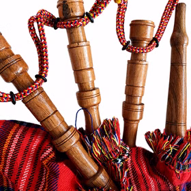 Dudelsack Holzpfeifen Detailansicht Detailaufnahme des Dudelsacks mit braunen Holzpfeifen, rot kariertem Luftsack, bunten Fransen und geflochtenen Schnüren.