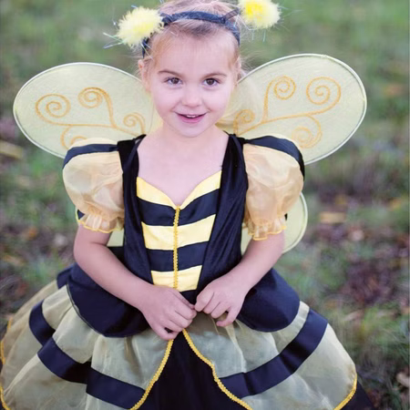 Bienen Kostüm Schwarz-Gelbes Kleid für Kinder 3-6 Jahre Tier Tierkostüm SALE Fasching Karneval Kindergeburtstag Mottoparty Kinderfasching Kind trägt ein schwarz-gelbes Bienenkostüm mit Flügeln und Haarreif und schaut lächelnd in die Kamera auf einer Wiese.