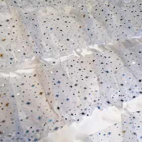 Detailansicht des transparenten Tüllstoffs mit glitzernden Stern- und Punktmotiven auf weißem Satinuntergrund, zeigt die Materialstruktur des Engel-Kostüms.